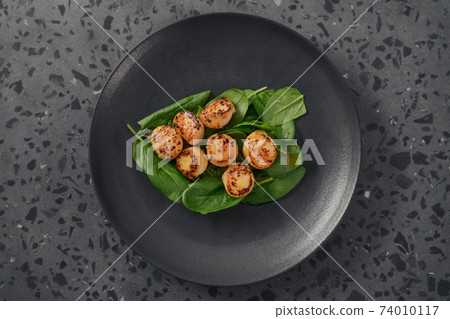 Seared scallops on pile of spinach on black plate top view Seared scallops on pile of spinach on black plate top view 74010117