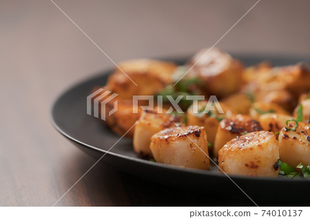Seared scallops on black plate closeup 74010137