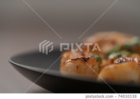 Seared scallops on black plate closeup 74010138