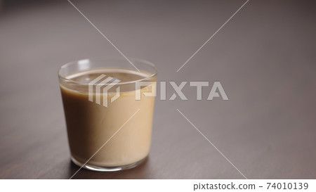milk pour into tumbler glass with coffee on walnut table milk pour into tumbler glass with coffee on walnut table 74010139