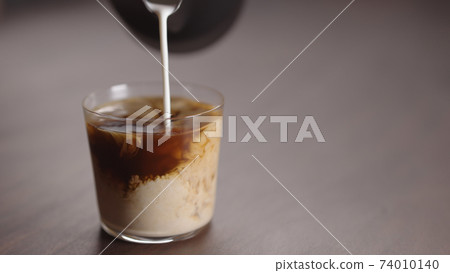 milk pour into tumbler glass with coffee on walnut table milk pour into tumbler glass with coffee on walnut table 74010140
