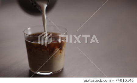 milk pour into tumbler glass with coffee on walnut table milk pour into tumbler glass with coffee on walnut table 74010146