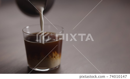 milk pour into tumbler glass with coffee on walnut table milk pour into tumbler glass with coffee on walnut table 74010147