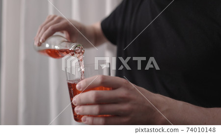 man pouring red drink into tumbler glass near window man pouring red drink into tumbler glass near window 74010148