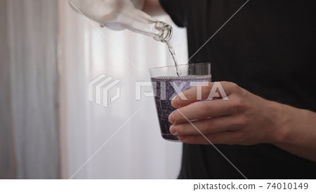 man pouring purple drink into tumbler glass near window man pouring purple drink into tumbler glass near window 74010149