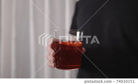 man drinking red drink from tumbler glass near window man drinking red drink from tumbler glass near window 74010151