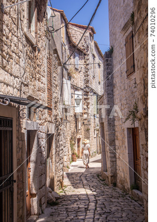 Rear view of beautiful blonde young female traveler wearing straw sun hat sightseeing and enjoying summer vacation in an old traditional costal town at Adriatic cost, Croatia Rear view of beautiful blonde young female traveler wearing straw sun hat sightseeing and enjoying summer vacation in an old traditional costal town at Adriatic cost, Croatia 74010296