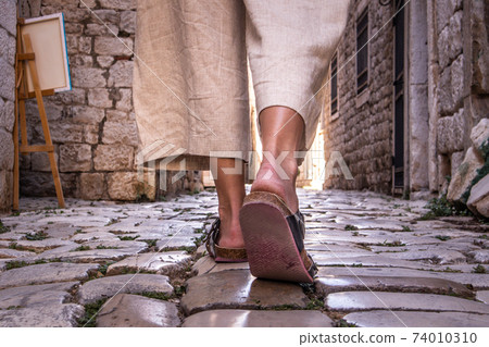 Detail shot of female legs wearing comfortable travel sandals walking on old medieval cobblestones street dring sightseeing city tour. Travel, tourism and adventure concept 74010310
