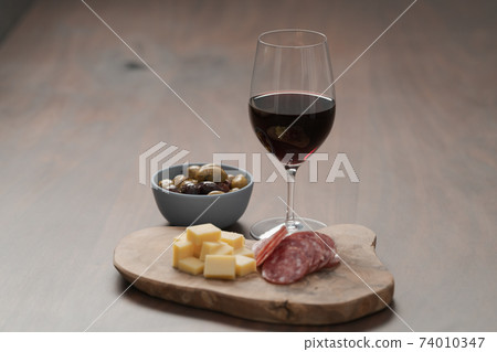olives, salami and vintage cheese with glass of red wine on walnut table 74010347