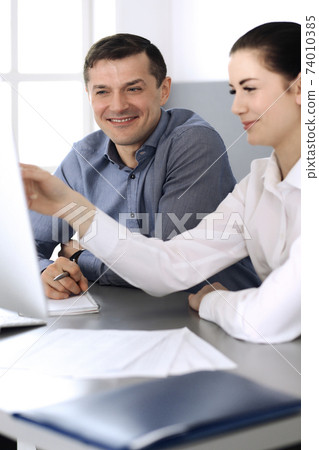 Cheerful smiling businessman and woman working with computer in modern office. Headshot at meeting or workplace. Teamwork, partnership and business concept 74010385