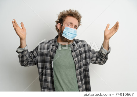 Young man in protective face mask with curly hair showing I don't know gesture with both hands isolated on white background. Portrait of confused sick young man on white background Young man in protective face mask with curly hair showing I don't know gesture with both hands isolated on white background. Portrait of confused sick young man on white background 74010667