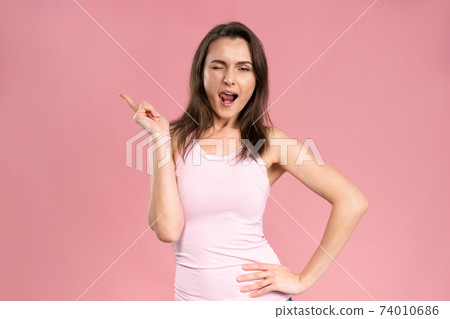 Playful, knowing something and winking looking at the camera young woman with dark hair in pink t-shirt holding hand on her waist. Facial expressions, emotions, feelings Playful, knowing something and winking looking at the camera young woman with dark hair in pink t-shirt holding hand on her waist. Facial expressions, emotions, feelings 74010686