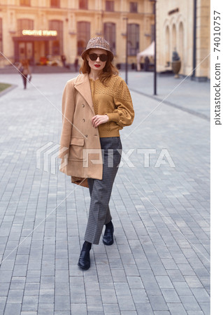 Outdoor portrait of charming spring time young french woman wearing sunglasses walking on camera with old town on background. Stylish female tourist standing at the city center square. Toned image Outdoor portrait of charming spring time young french woman wearing sunglasses walking on camera with old town on background. Stylish female tourist standing at the city center square. Toned image 74010757