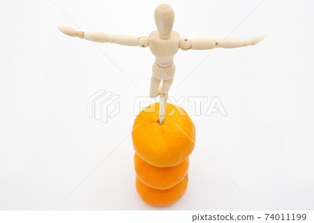 A drawing figure that balances on a pile of oranges 74011199