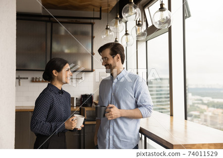 Happy mixed race couple drink tea coffee by picture window 74011529
