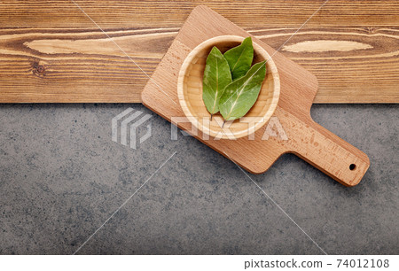 The bay leaves on cutting board set up on shabby wooden background with copy space . 74012108