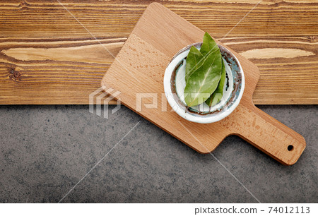 The bay leaves in ceramic bowl on shabby wooden background with copy space . 74012113