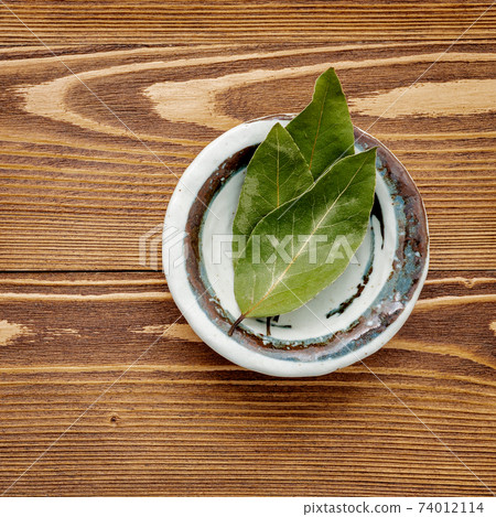 The bay leaves in ceramic bowl on shabby wooden background with copy space . 74012114