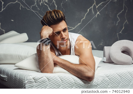Man lying on a white pillow and a mattress on a gray background. Concept of comfortable sleep. orthopedic mattress and pillow Man lying on a white pillow and a mattress on a gray background. Concept of comfortable sleep. orthopedic mattress and pillow 74012940