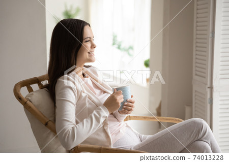 Happy young woman relax in chair drinking tea 74013228