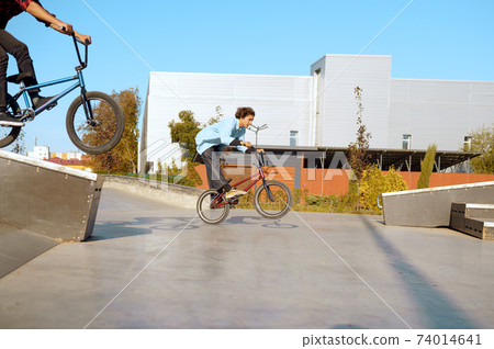 Two male bmx bikers doing tricks in skatepark Two male bmx bikers doing tricks in skatepark 74014641
