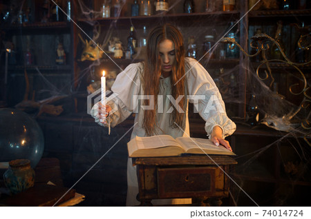Demonic woman with candle reads book of spells Demonic woman with candle reads book of spells 74014724