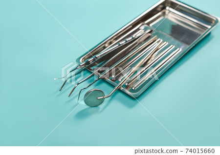Steel dental tools on a blue background. Dental mirror, forceps extractor, scaler, cotton pliers 74015660