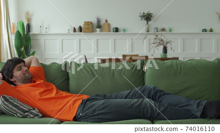 Happy man is resting on a comfortable sofa, resting with his eyes closed 74016110