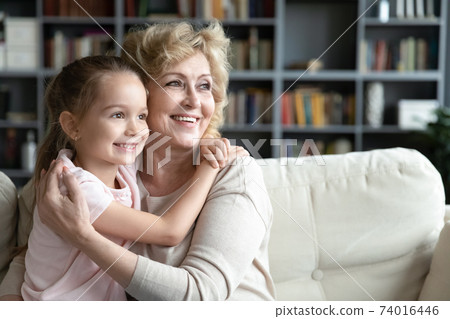 Smiling little girl cuddling loving caring older middle aged grandmother. 74016446