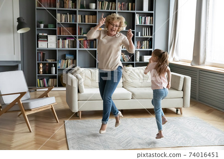 Overjoyed mature senior grandmother dancing with little girl. Overjoyed mature senior grandmother dancing with little girl. 74016451