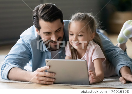 Smiling young father watching cartoons on tablet with small daughter. 74016508