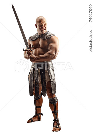 Severe barbarian in leather costume with sword. Portrait of balded muscular gladiator. Studio shot. Isolated on white background Severe barbarian in leather costume with sword. Portrait of balded muscular gladiator. Studio shot. Isolated on white background 74017040