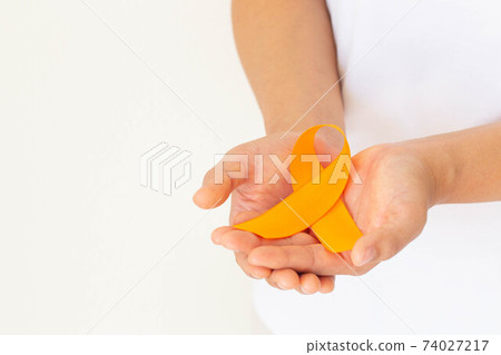 Hands holding orange color ribbon on white fabric with copy space. Kidney Cancer Awareness, Leukemia disease, Skin cancer awareness, World Cancer Day. Healthcare or hospital and insurance concept. 74027217