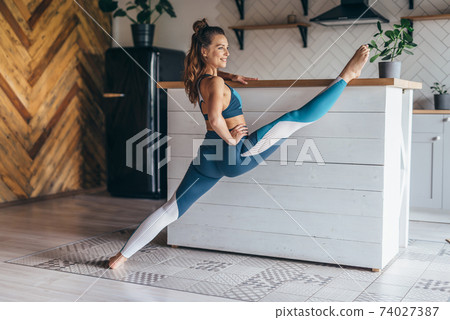 Fit woman does a stretching exercise with her leg up on the table. 74027387