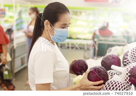 Asian woman long hair wearing protective face mask in supermarket department store. Female, looking grocery to buy some fruit. New normal after covid-19. Family concept. Asian woman long hair wearing protective face mask in supermarket department store. Female, looking grocery to buy some fruit. New normal after covid-19. Family concept. 74027910