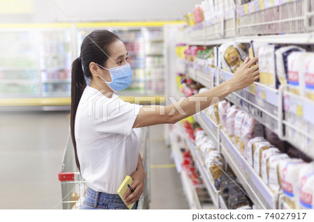 Asian woman wear face mask push shopping cart in supermarket. female looking grocery to buy something During coronavirus crisis or covid19 outbreak. Women wearing protective face mask new normal 74027917