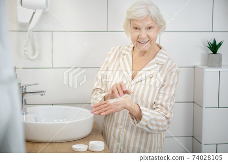 Elderly smiling woman applying hand cream on hands Elderly smiling woman applying hand cream on hands 74028105