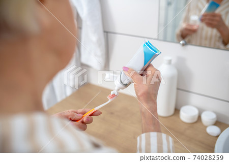 Close up picture of a woman squeezing toothpaste an a toothbrush Close up picture of a woman squeezing toothpaste an a toothbrush 74028259