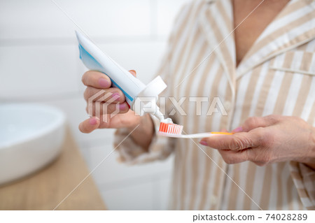Close up picture of a woman squeezing toothpaste an a toothbrush 74028289