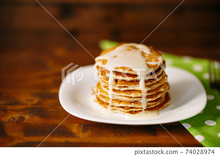 Condenced milk being poured on a stack of pancakes. 74028974