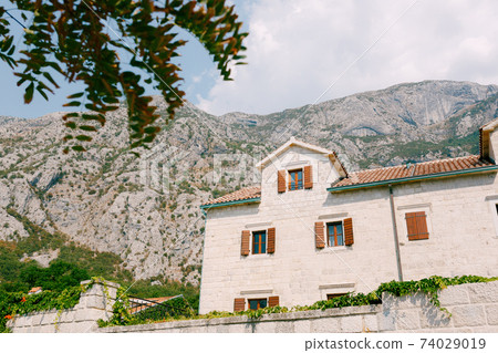 An ancient white building with windows and wooden shutters against the backdrop of mountains. An ancient white building with windows and wooden shutters against the backdrop of mountains. 74029019