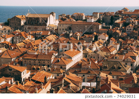 Roofs of the old city of Dubrovnik, orange roof tiles on houses, a view from a height, from the wall. Domes of The Church of the Holy Annunciation and St. Ignatius Church. Roofs of the old city of Dubrovnik, orange roof tiles on houses, a view from a height, from the wall. Domes of The Church of the Holy Annunciation and St. Ignatius Church. 74029031