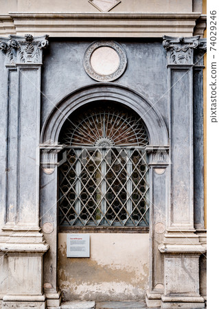 Arched window with a metal lattice in the opening between the columns with patterns. 74029246