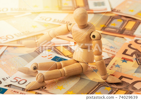 Wooden mannequin sits on the euro currency Wooden mannequin sits on the euro currency 74029639