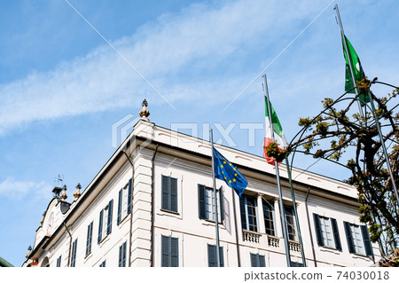 Flag of the European Union and Italy on high flagpoles in front of a multi-storey building. 74030018