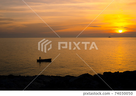 A fisherman on a boat near the shore against the backdrop of a golden sunset. 74030050
