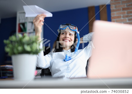 Woman in diving mask launching paper plane at office 74030852