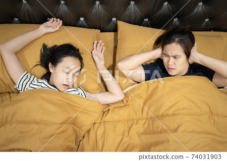 Asian teen daughter snoring with open mouth,mother is closing ears with hands,loud noise,annoying snoring of child girl,risk of sleep apnea while sleeping,unhappy woman wakes up while lying in the bed 74031903