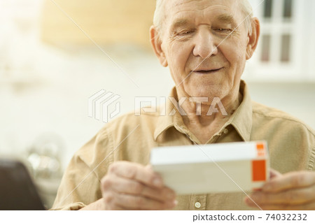 Attentive grandpa checking the name of his medication on box Attentive grandpa checking the name of his medication on box 74032232