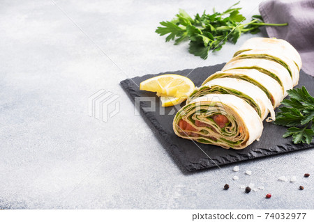 Rolls of thin pita bread and red salted salmon with lettuce leaves On a slate stand, grey concrete background. Copy space. Rolls of thin pita bread and red salted salmon with lettuce leaves On a slate stand, grey concrete background. Copy space. 74032977
